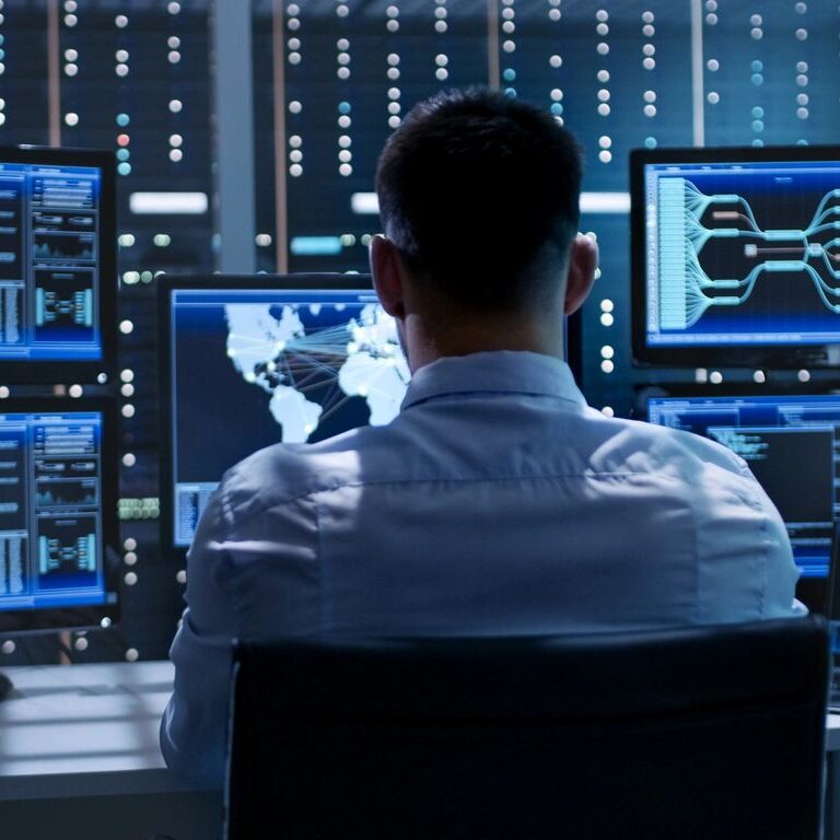 Man analyzing multiple digital data screens in a tech control room.
