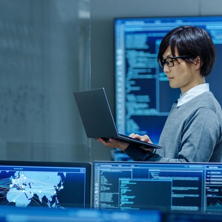 A professional analyzing data on multiple screens in a tech environment.