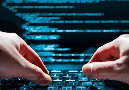 Hands typing on a keyboard with blue code on screen.